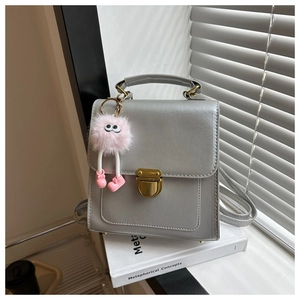 Detail of silver faux leather crossbody bag with vintage gold lock and pink plush charm