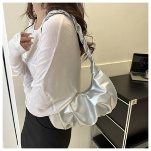 Silver metallic dumpling bag with pleated design and woven strap shown on shoulder