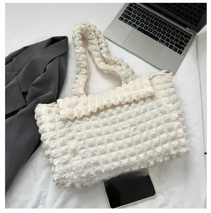 Size comparison of a quilted bubble tote bag next to a smartphone in a lifestyle setting
