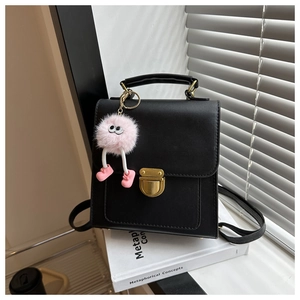 Detail of black matte leather handbag with gold metal lock and pink plush charm