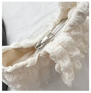 Detail of silver zipper closure on a white pleated bubble puff shoulder bag texture
