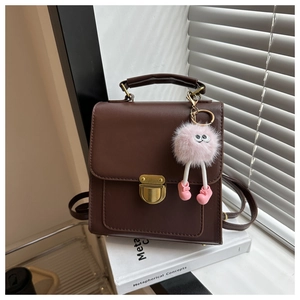 Detail of dark brown leather backpack with golden lock and pink plush monster charm
