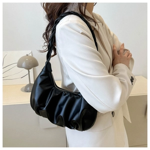 Close-up of black pleated cloud bag with woven handle carried by a model in a suit