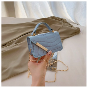 Detail of light blue croc-embossed handbag with gold chain strap and metal trim