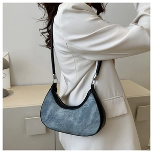 Detail of crescent denim shoulder bag with leather trim and gold logo on white blazer