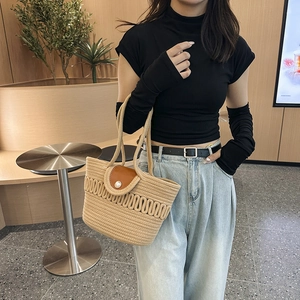 Beige woven tote bag with brown leather flap and pearl detail held by a model
