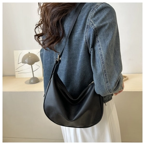 Close-up of black lychee grain hobo bag worn with a denim jacket and white skirt