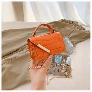 Detail of bright orange crocodile texture mini bag with gold chain strap and metal trim
