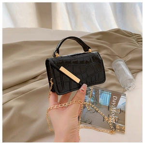 Detail shot of black crocodile embossed mini bag with gold chain and metal hardware bar
