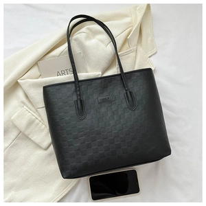 Détail du sac cabas noir avec texture tressée, étiquette en cuir et bandoulières