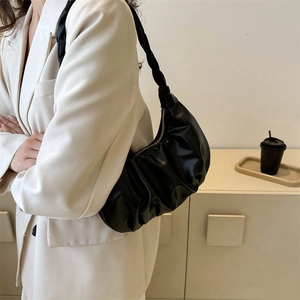 Minimalist black pleated cloud bag with woven handle shown on shoulder in casual setting