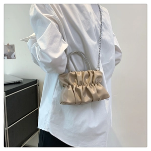 Detail showing the rhinestone circular handles and draped silver chain on the beige ruched bag