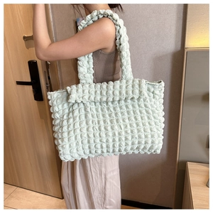 Detail of light green bubble texture tote bag worn by a model in an indoor setting