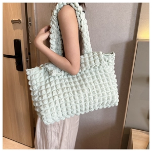 Detail of mint green puffed texture shoulder bag worn by model in a cozy indoor setting