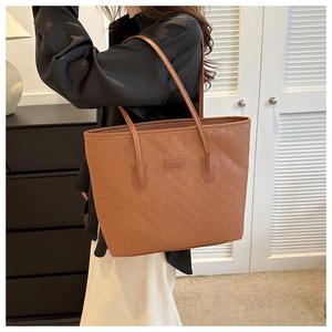 Détail du sac cabas tressé marron avec écusson Fashion porté à l'épaule pour le style