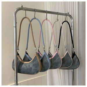 Five denim crescent underarm bags in various colors hanging on a stainless steel rack