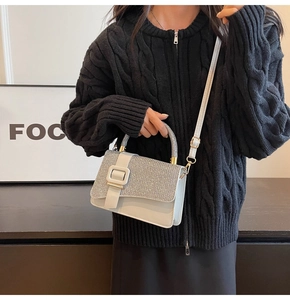 Detail of white leather crossbody bag featuring silver glitter flap and adjustable strap