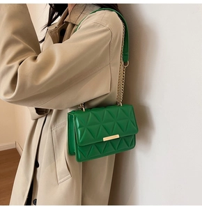 Detail of green quilted crossbody bag with golden metal clasp and chain strap on trench coat