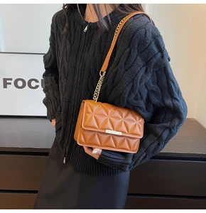 Close-up of brown quilted shoulder bag with gold chain and metal lock on knit sweater