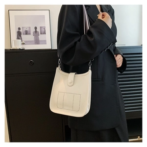 Detail of off-white bucket bag featuring perforated H pattern and striped webbing strap