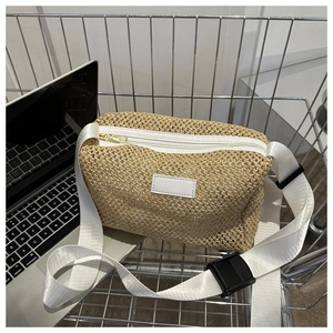 Détail d'un sac bandoulière en paille tressée avec sangle en nylon blanc dans un panier