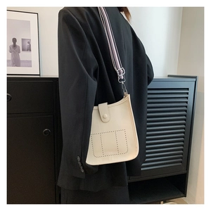Detail of cream bucket bag with perforated circular patterns and striped wide shoulder strap