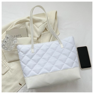 Detailed view of white quilted tote bag with faux leather trim on a stylish setting
