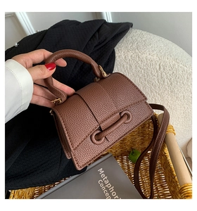 Brown litchi grain leather handbag with round handle and strap in a woven basket