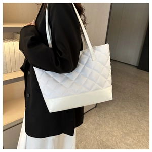 Detailed view of white quilted tote bag worn by a model in a minimalist setting