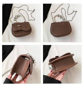Detail van bruine tas met steenpatroon, hartvormige zilveren kralen en parelketting