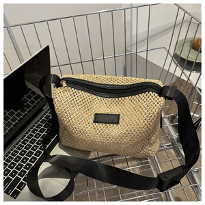 Détail d'un sac bandoulière en paille avec sangle en nylon noir et écusson en cuir