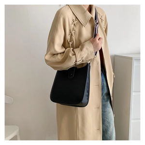 Close-up of black litchi pattern bucket bag with striped fabric shoulder strap on a model