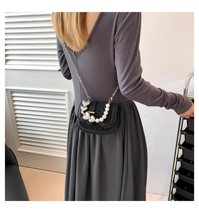 Detail van zwarte geweven crossbodytas met hartvormige hanger en elegante parelketting