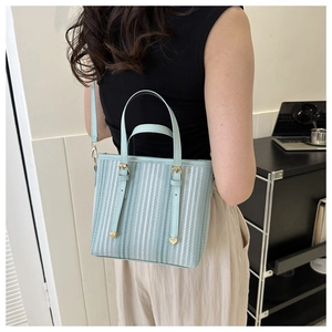 Close-up of stylish light blue striped bucket bag worn as a crossbody on a model
