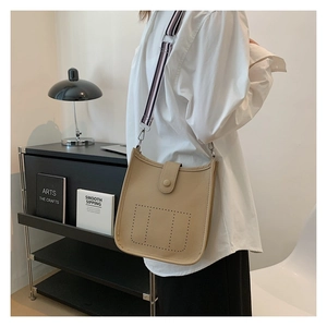 Detail of khaki bucket bag with perforated H design and striped woven shoulder strap