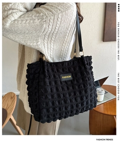 Detail of black puffer tote bag with bubble texture and yellow fashion label on shoulder