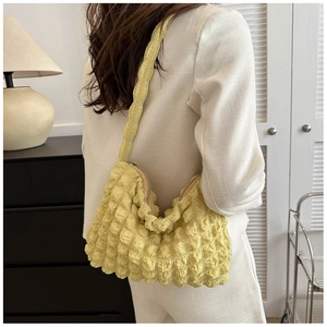 Détail du tissu à bulles texturé et de la forme en croissant du sac jaune sous le bras
