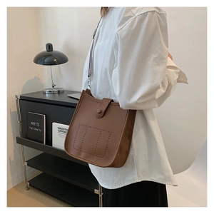 Brown leather bucket bag with perforated design and wide fabric strap worn by a model