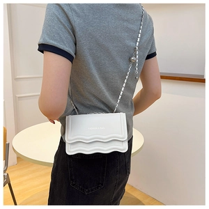 Detailed view of white crossbody bag with wave texture edge and silver metal chain strap