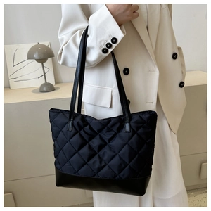 Close-up of a black quilted tote bag with leather straps on a model in a minimal setting