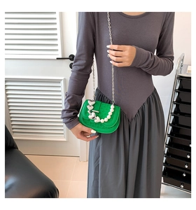 Detail van groene tas met steentextuur, zilveren hartbedel en parelketting decoratie