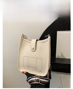 Close-up of white lychee leather bucket bag with perforated design and striped strap