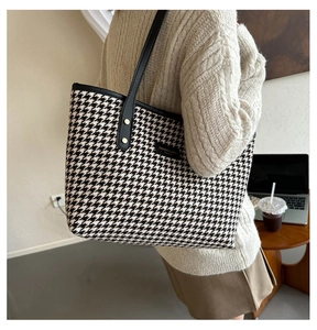 Detail of checkered tote bag with leather straps and gold studs in a cozy office setting