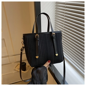 Close-up of black striped woven tote bag featuring gold buckles and vegan leather trim