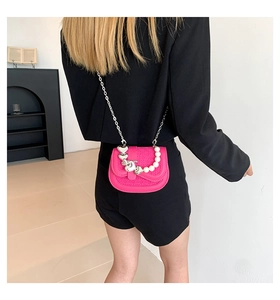 Detail van rozerode crossbodytas met zilveren hartjes en een parelketting voor dames