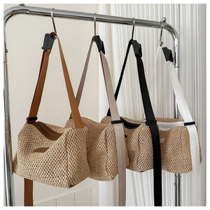 Détail de quatre sacs bandoulière en paille avec différentes sangles suspendus au support