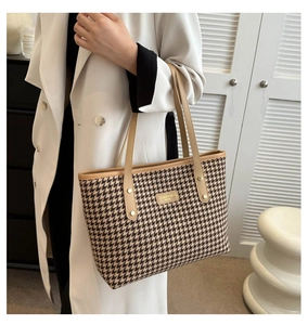 Detail of houndstooth tote bag with brown leather trim and golden logo plate