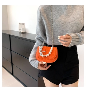 Detail van oranje geweven tas met parelketting en zilveren hartvormige hanger