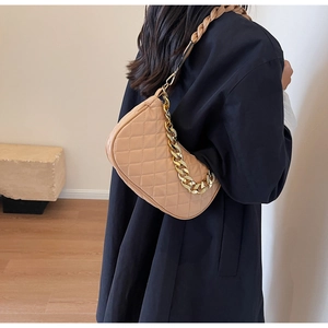 Dettaglio borsa beige trapuntata con catena dorata indossata da modella in un contesto minimalista