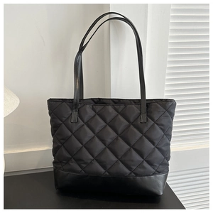 Close-up of black quilted tote bag with large diamond stitching and leather base detail